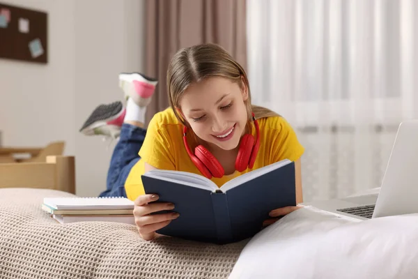 Online Tanulás Tini Lány Olvasás Könyv Közelében Laptop Ágyon Otthon — Stock Fotó