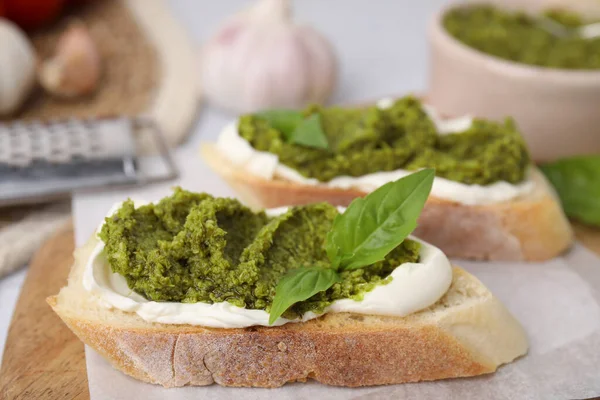 Krem peynirli lezzetli bruschettalar, pesto sosu ve ahşap tahtada taze fesleğen, yakın plan.