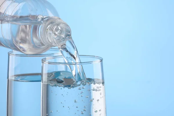 stock image Pouring water from bottle into glass on light blue background, closeup. Space for text