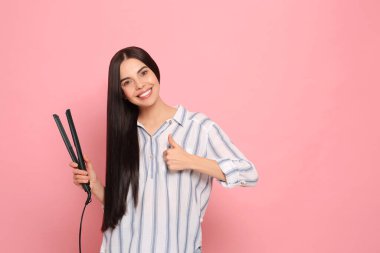 Pembe arka planda saç ütüsü olan güzel, mutlu bir kadın. Metin için boşluk