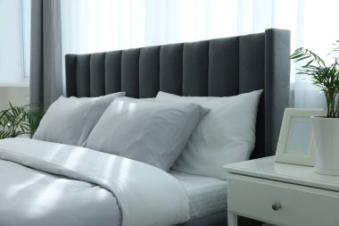 Odadaki beyaz komodinin üzerinde rahat bir yatak ve yeşil bir çiçek. Şık iç mekan