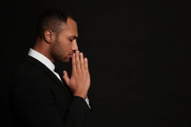 Siyah arka planda Tanrı 'ya dua eden elleri sımsıkı bağlı Afrikalı Amerikalı bir adam. Metin için boşluk