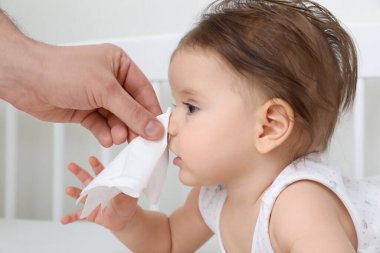 Baba küçük bebeğin burnunu peçeteyle siliyor, yakın plan.