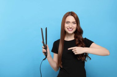 Açık mavi arka planda saç maşasını gösteren güzel bir kadın. Metin için boşluk