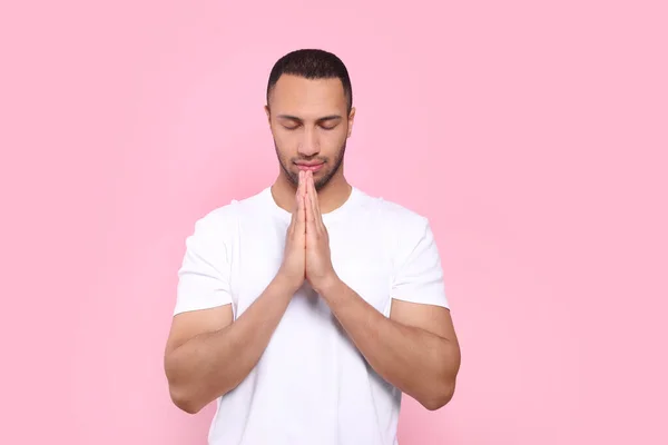 African American man with clasped hands praying to God on pink background