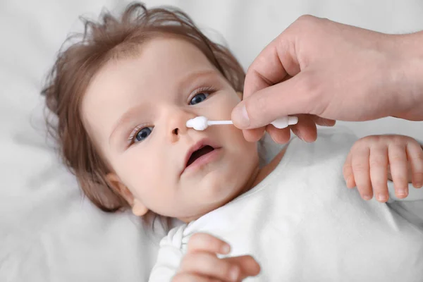stock image Father cleaning nose of his baby with cotton bud on bed, closeup