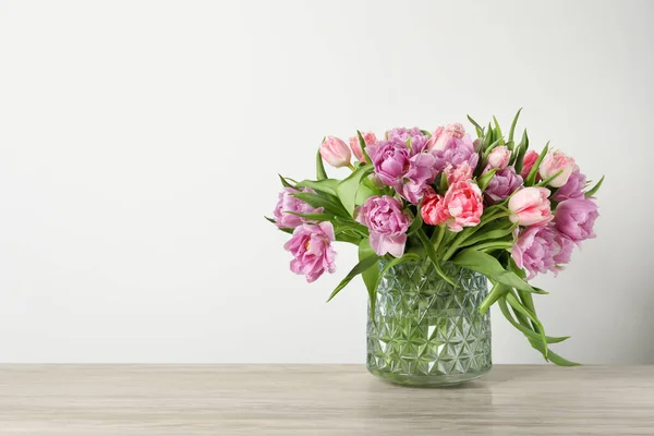 stock image Beautiful bouquet of colorful tulip flowers on wooden table near light wall, space for text