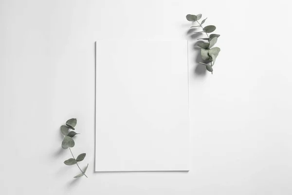 stock image Empty sheet of paper and decorative eucalyptus leaves on white background, flat lay. Mockup for design