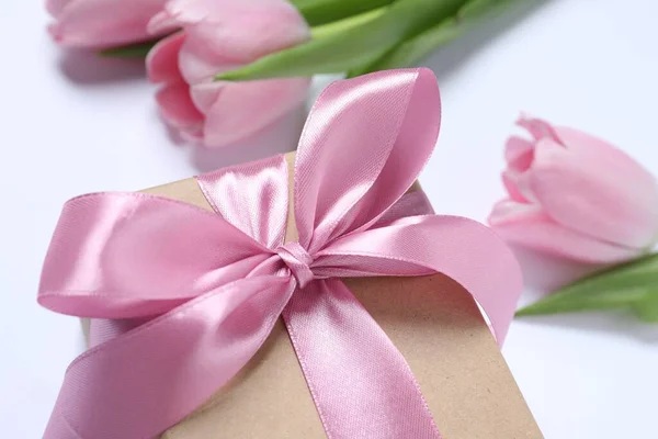 Beautiful gift box with pink bow and tulips on white background, closeup