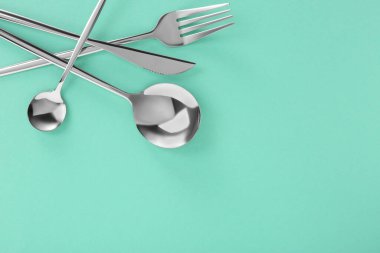 Çatal, bıçak ve kaşık turkuaz arka planda, düzlük ve metin için boşluk. Şık çatal bıçak takımı