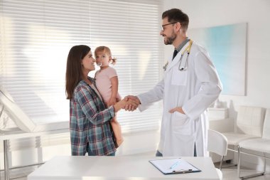 Annesi ve sevimli bebeğinin klinikteki çocuk doktoruyla randevusu var. Doktor küçük kızı muayene ediyor.