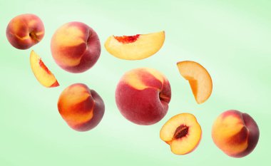 Açık yeşil zemine düşen taze şeftali kesimi ve taze olgun şeftaliler.