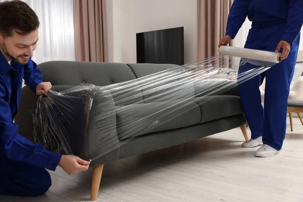 Male Movers Stretch Film Wrapping Sofa New House — Stockfoto