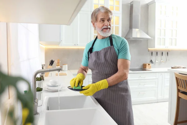 穿着防护手套的老人在厨房洗碗槽上方洗盘子 — 图库照片