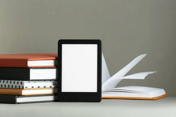 Modern e-book reader and hard cover books on light grey table