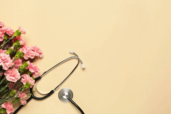 Stethoscope and beautiful carnation flowers on beige background, flat lay with space for text. Happy Doctor\'s Day