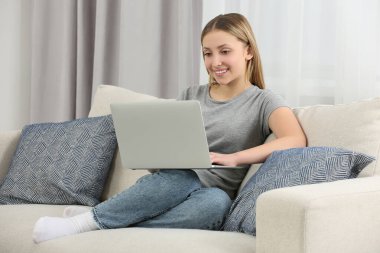 Teenage girl using laptop on sofa at home