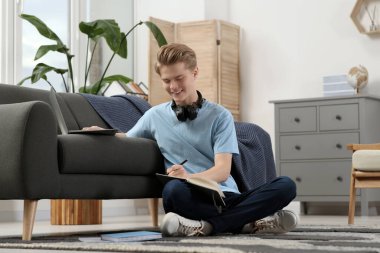 Çevrimiçi öğrenme. Gülümseyen genç çocuk evde dizüstü bilgisayarın yanında kompozisyon yazıyor.