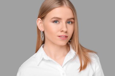 Gri arka planda zarif küpeleri olan güzel genç bir kadın.