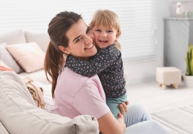Mother with her cute little daughter on sofa at home, space for text