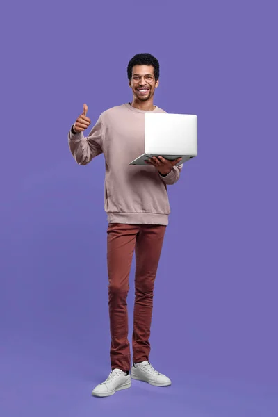 笑顔男とノートパソコンの上に親指を表示紫色の背景 — ストック写真