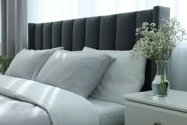 白いベッドサイドテーブルの上に美しい花と部屋の快適なベッドと花瓶 スタイリッシュなインテリア — ストック写真