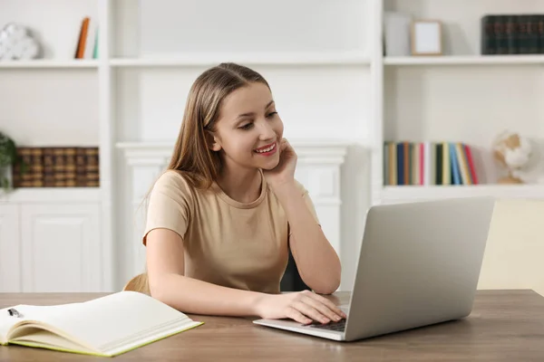 在线学习 在屋里的木桌边 拿着笔记本电脑笑着的少女 — 图库照片