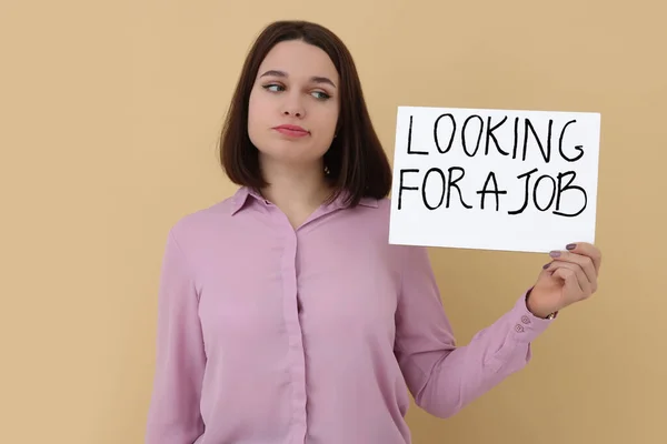 拿着标语牌的年轻失业妇女寻找米色背景的工作 — 图库照片