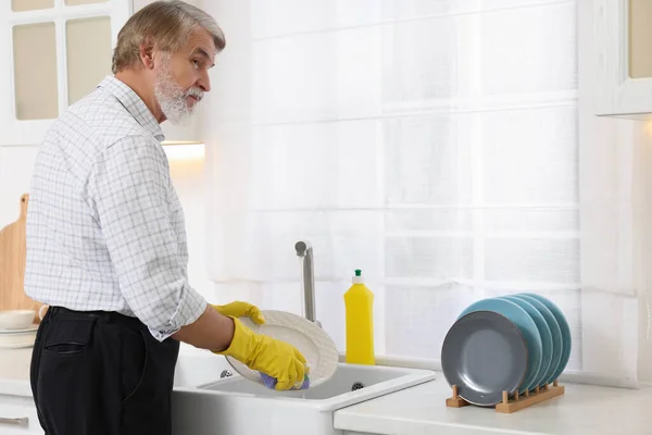 穿着防护手套的老人在厨房的洗碗槽上洗盘子 放文字的地方 — 图库照片