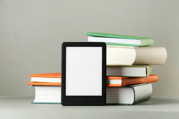 Modern e-book reader and stack of hard cover books on light grey table