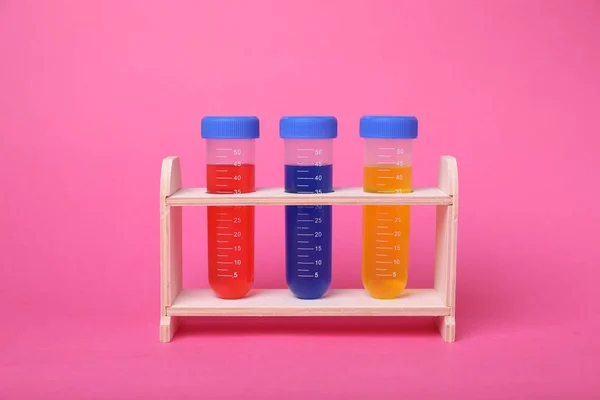 鮮やかなピンクの背景に木製のスタンドでカラフルな液体と試験管 子供の化学実験セット — ストック写真