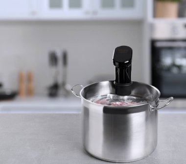 Sous vide cooker and vacuum packed food products in pot on light marble table in kitchen, space for text. Thermal immersion circulator clipart