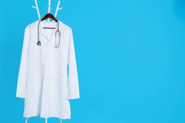Beyaz tıbbi üniforma ve steteskop açık mavi arka planda asılı duruyor. Metin için boşluk