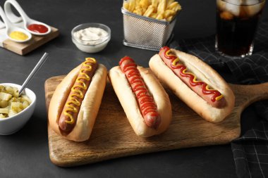 Fresh delicious hot dogs with sauces served on black table clipart