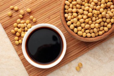 Soya sosu kasede ve soya fasulyesi bej masada, düz yerde.