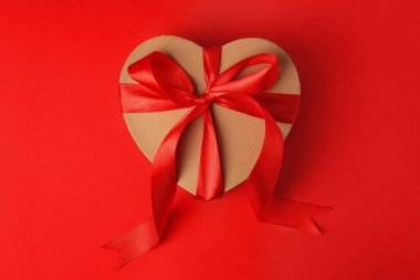 Güzel kalp şeklinde hediye kutusu, kırmızı arka planda fiyonk, üst manzara.