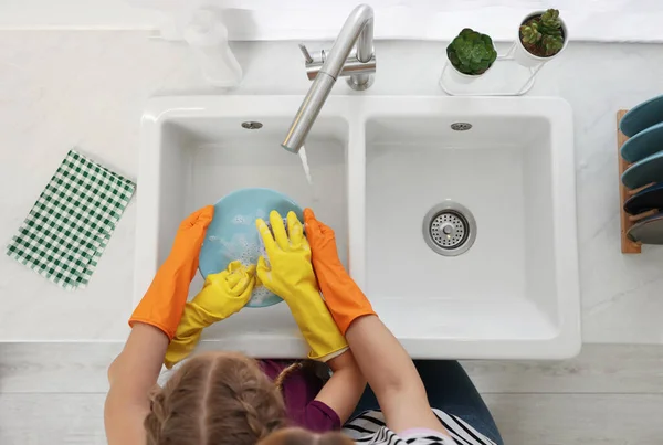 母亲和女儿戴着防护手套洗碗盘在水池上方 — 图库照片