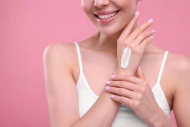 Elinde krem lekesi olan bir kadın pembe arka planda, yakın plan.