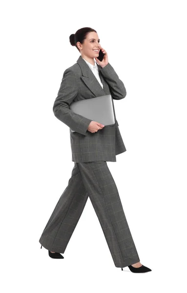 白い背景を背景に歩いている間 スマートフォンで話しているラップトップを持つ美しい幸せなビジネス女性 — ストック写真
