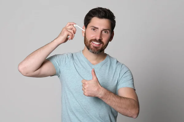 耳のスプレーを使用してグレーの背景に親指を表示する男 — ストック写真