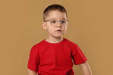 Soluk kahverengi arka planda gözlüklü şirin bir çocuk.