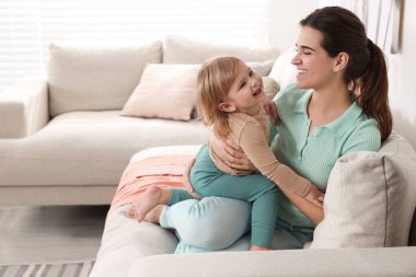 Mother with her cute little daughter on sofa at home, space for text