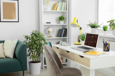 Modern dizüstü bilgisayarı beyaz ahşap masa ve evdeki rahat koltuğu olan rahat çalışma alanı.