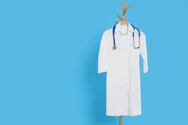 stock image White medical uniform and stethoscope hanging on rack against light blue background. Space for text