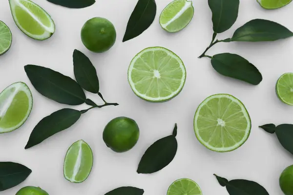 stock image Whole and cut fresh limes with leaves on white background, flat lay