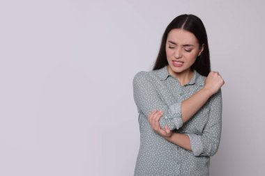 Dirseğindeki acıdan muzdarip genç bir kadın açık gri arka planda, mesaj için yer var. Artrit belirtileri