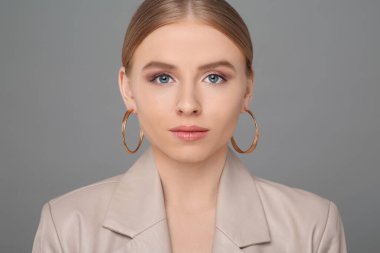 Gri arka planda zarif küpeleri olan güzel genç bir kadın.