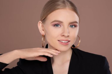 Açık kahverengi arka planda zarif küpeleri olan güzel genç bir kadın.