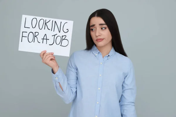 拿着标语牌的年轻失业妇女在灰色背景下寻找工作 — 图库照片