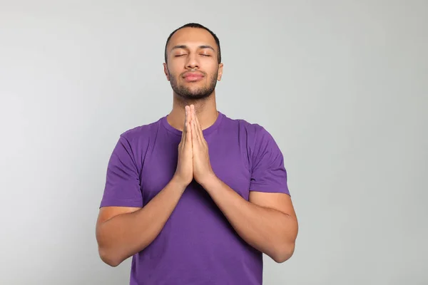 stock image African American man with clasped hands praying to God on light grey background